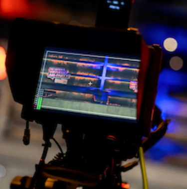 Monitor einer Kamera zeigt die Live-Aufnahme eines „Virtuelle Abi-Party“-Schilds bei bunter Bühnenbeleuchtung.