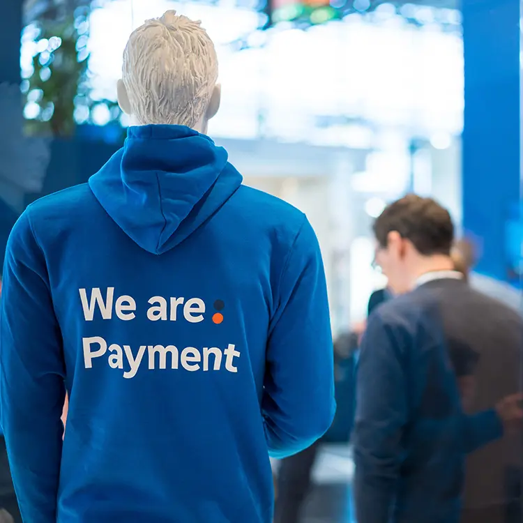 Rückenansicht einer Schaufensterpuppe mit blauem Hoodie und Aufdruck „We are: Payment“.