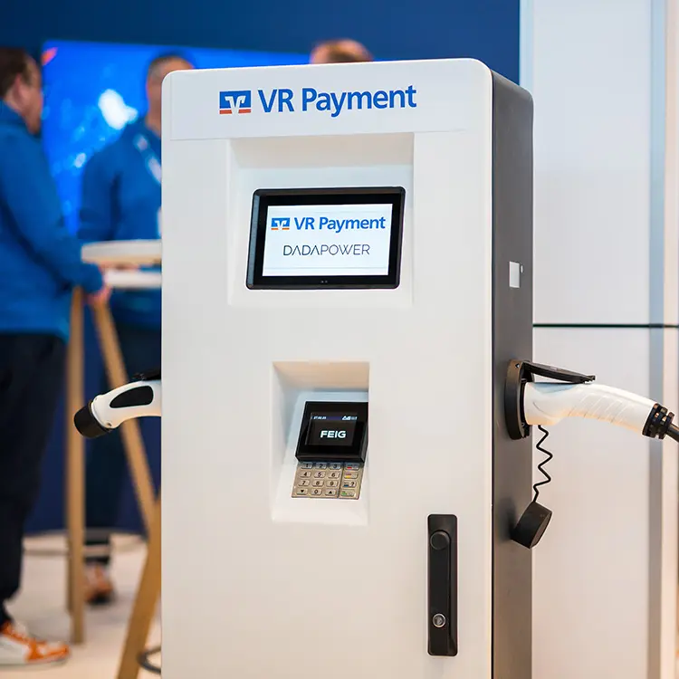 VR Payment-Ladesäule mit Display, Kartenterminal und zwei angeschlossenen Ladekabeln auf einer Messe.