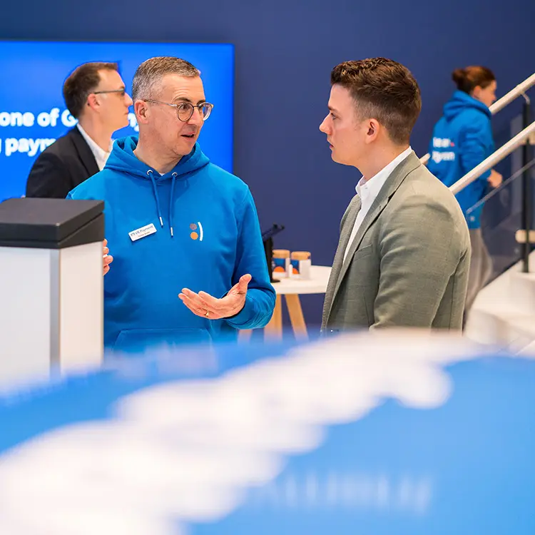 Mitarbeiter im blauen VR Payment-Hoodie im Gespräch mit einem jungen Mann auf einem Messestand.
