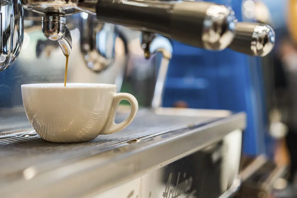 Espressomaschine füllt frischen Kaffee in eine weiße Tasse auf dem Abtropfgitter.