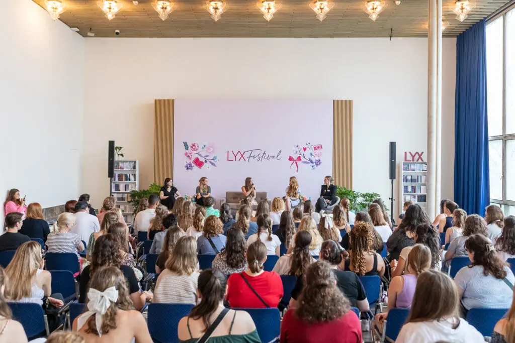 Publikum verfolgt einen Live-Book-Talk auf dem LYX Festival mit fünf Sprecherinnen vor blumiger Bühnenkulisse.