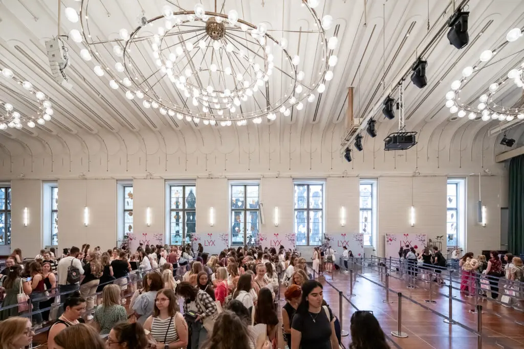 Großer Saal mit wartenden Besucher*innen in Absperrgittern unter prunkvollem Kronleuchter bei den Signierstunden auf dem LYX Festival.