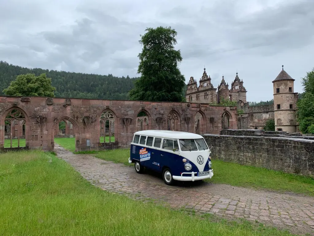 VW Bulli mit Morgen-kann-kommen Volksbanken Raiffeisenbanken Branding und Promotion-Stand mit Liegestühlen und Theke vor einer Burgmauer