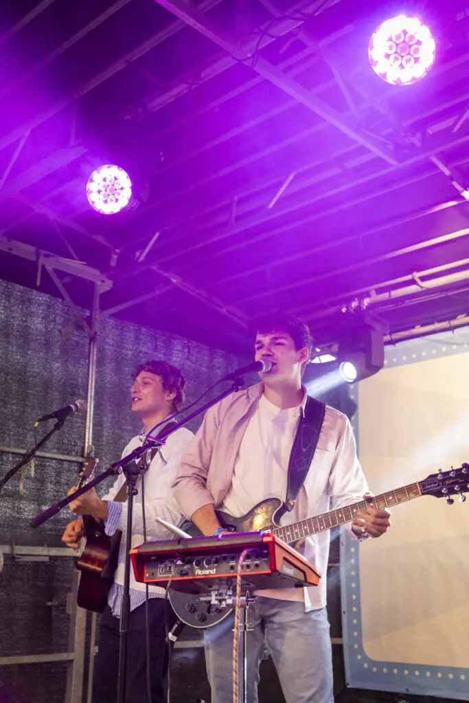 Zwei Musiker der Pup-Up-Boys auf einer Bühne unter violettem Scheinwerferlicht, beide mit Gitarren und Mikrofonen; im Vordergrund ein Keyboard auf einem Ständer.