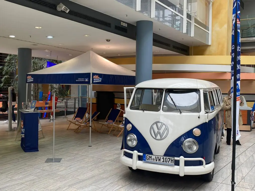 VW Bulli mit Morgen-kann-kommen Volksbanken Raiffeisenbanken Branding und Promotion-Stand mit Liegestühlen und Theke indoor.
