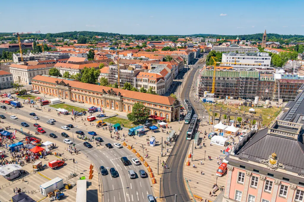 Weitwinkelaufnahme des Neuen Lustgartens in Potsdam mit Blick auf das bunte Festgelände zum Tag des Bevölkerungsschutzes. Links viele Infozelte und Einsatzfahrzeuge, rechts historische Gebäude und eine belebte Straße mit Baustelle.