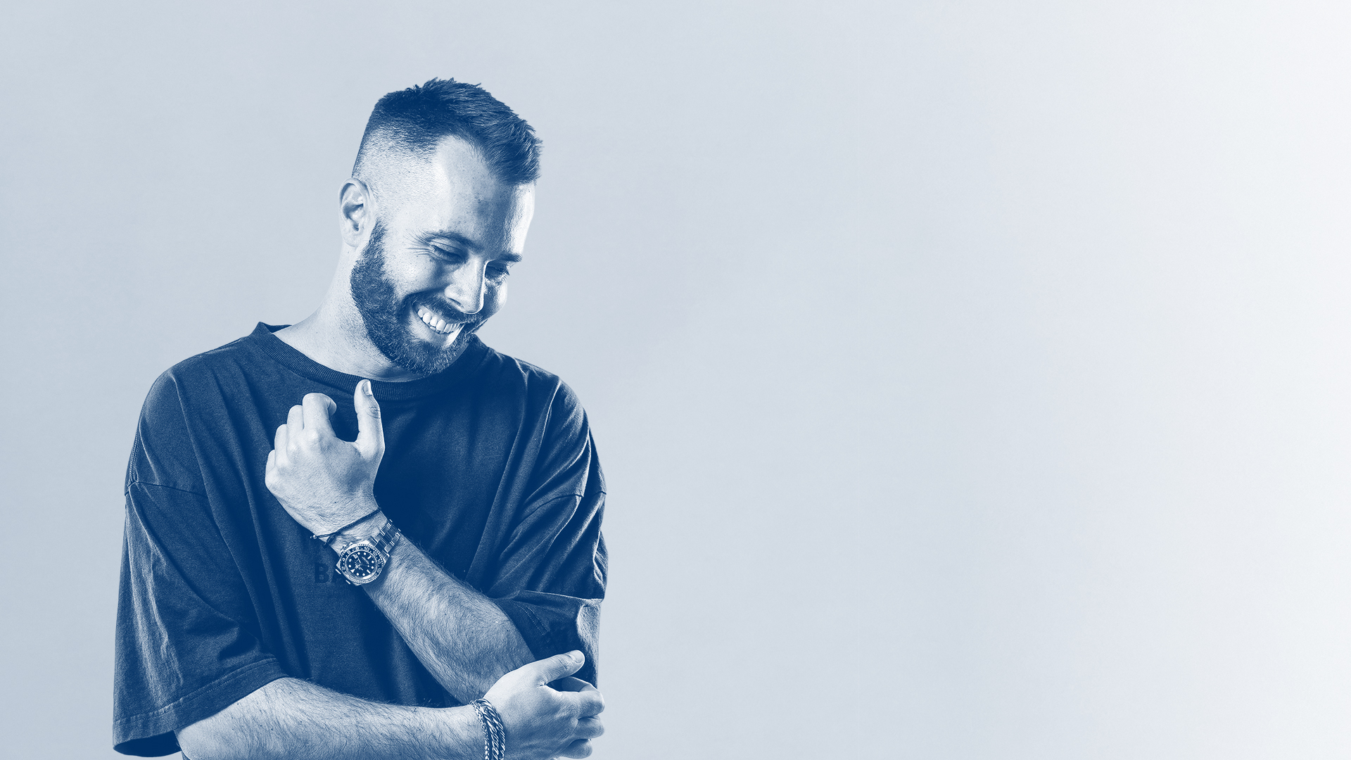 DJ David Puentez lacht und blickt nach unten; monochromes Porträt mit hellem Hintergrund.