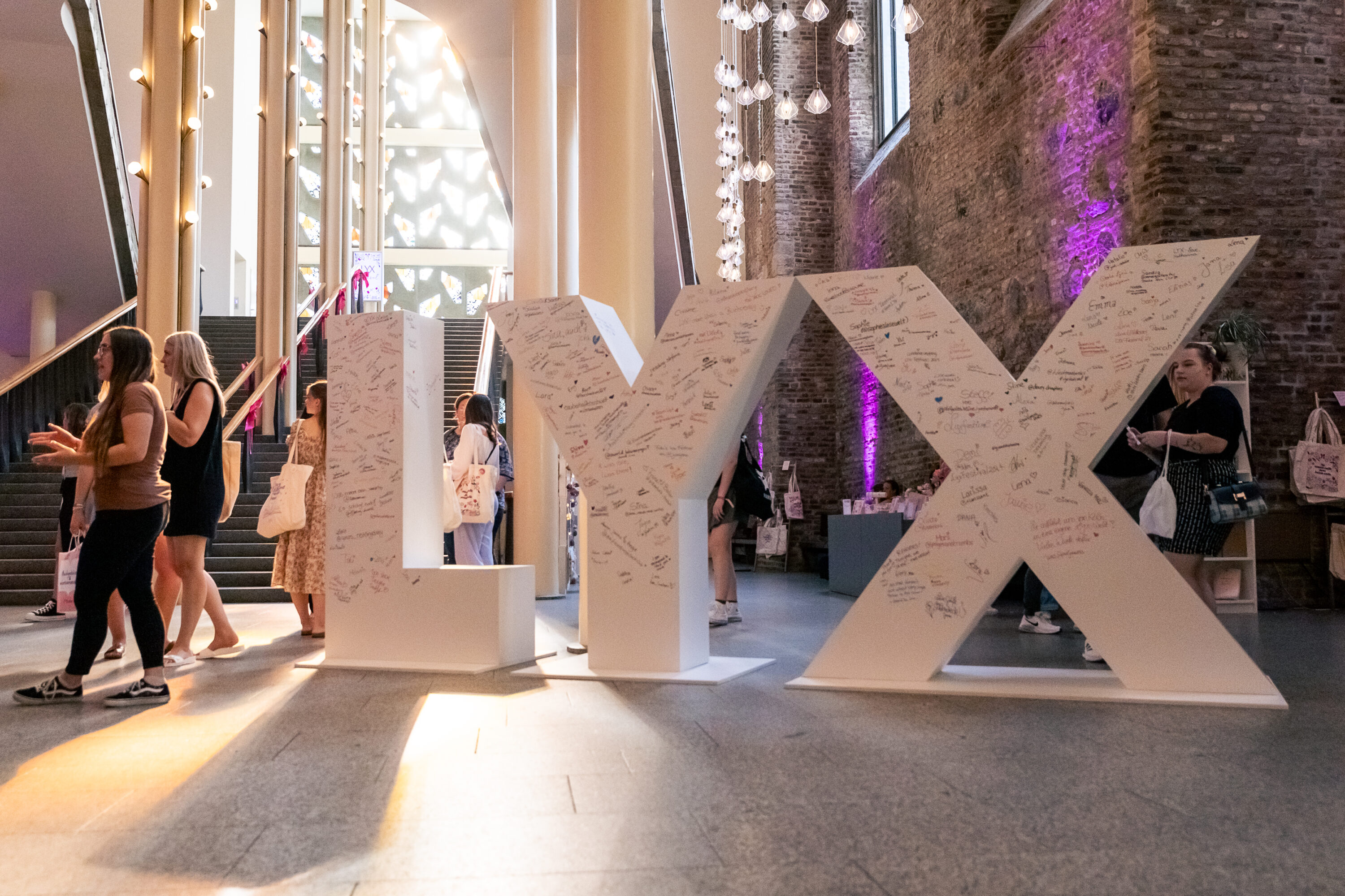 Große, weiße 3D-Buchstaben „LYX“ mit vielen Unterschriften, umgeben von Besucherinnen in einem modern-beleuchteten Eventraum.