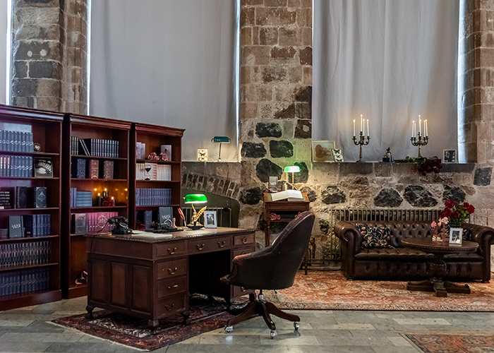 Dark-Academia-Setting mit antikem Schreibtisch, Bücherregalen, Chesterfield-Sofa und Kerzenleuchtern vor Steinwand.