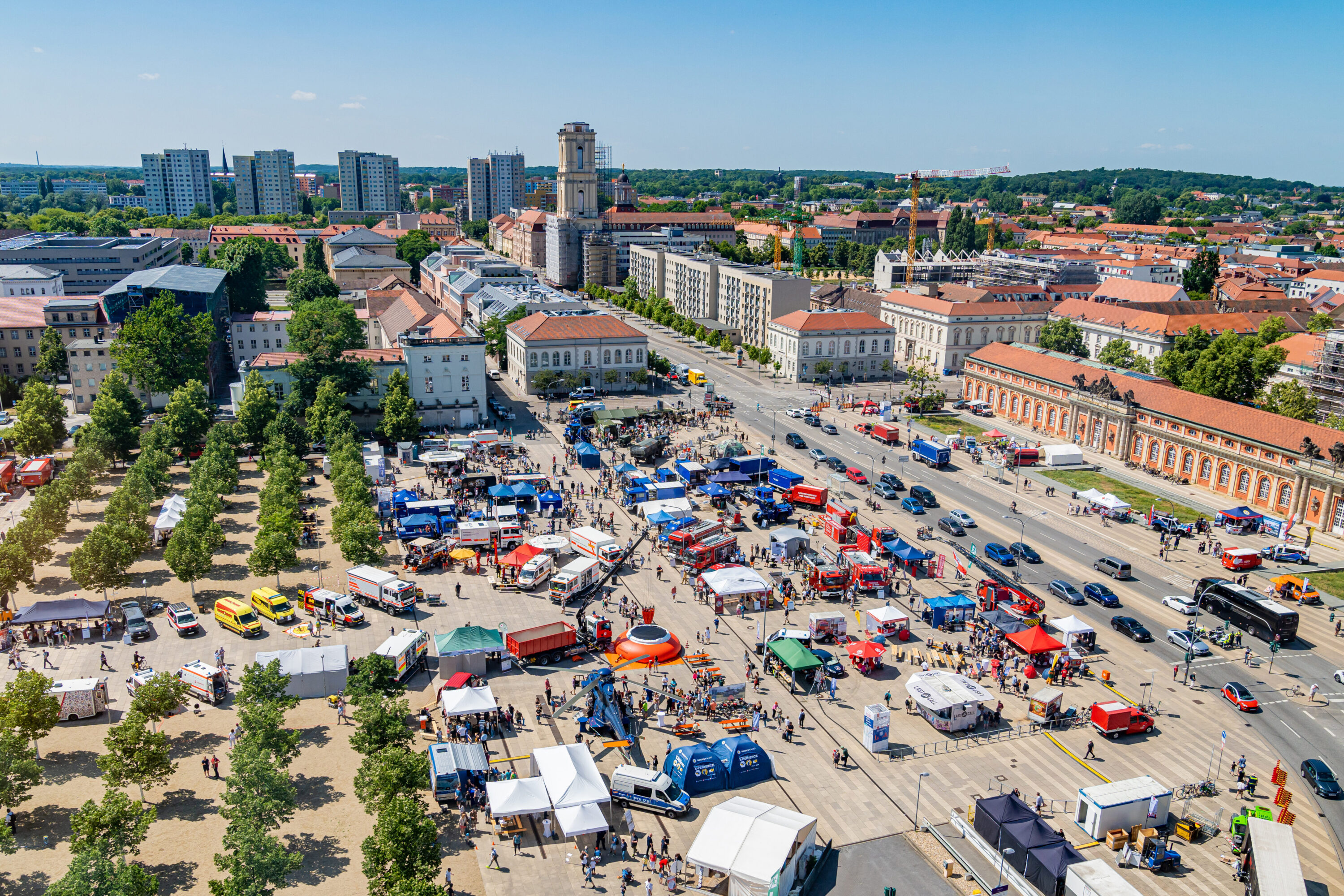Luftaufnahme des Neuen Lustgartens in Potsdam beim Tag des Bevölkerungsschutzes – zahlreiche Einsatzfahrzeuge, bunte Infostände und Besuchergruppen verteilen sich auf dem Platz vor historischer Kulisse und unter blauem Himmel.
