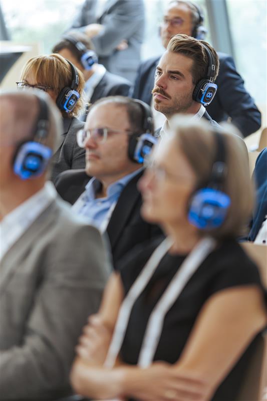 Zuhörende mit blauen Silent-Conference-Kopfhörern verfolgen aufmerksam eine Präsentation.