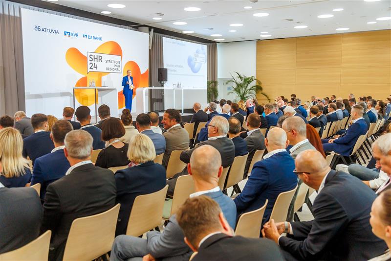 Großes Publikum hört einer Rednerin auf der SHR 24-Bühne in einem Konferenzraum zu.