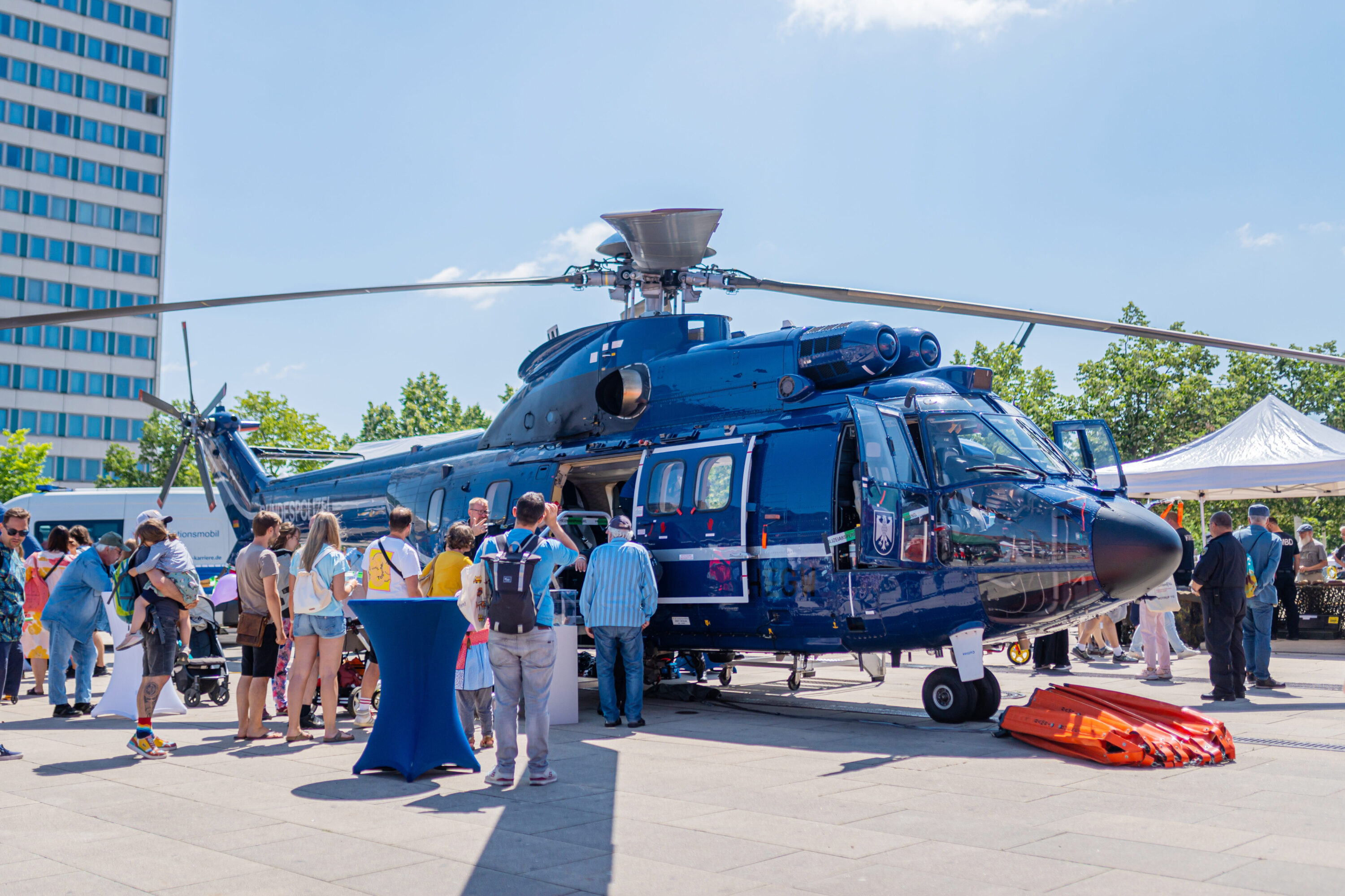 Ein dunkelblauer Polizei-Hubschrauber steht am Boden, umringt von Besucher*innen beim Tag des Bevölkerungsschutzes. Menschen schauen neugierig ins Cockpit und informieren sich rund um das Fluggerät.