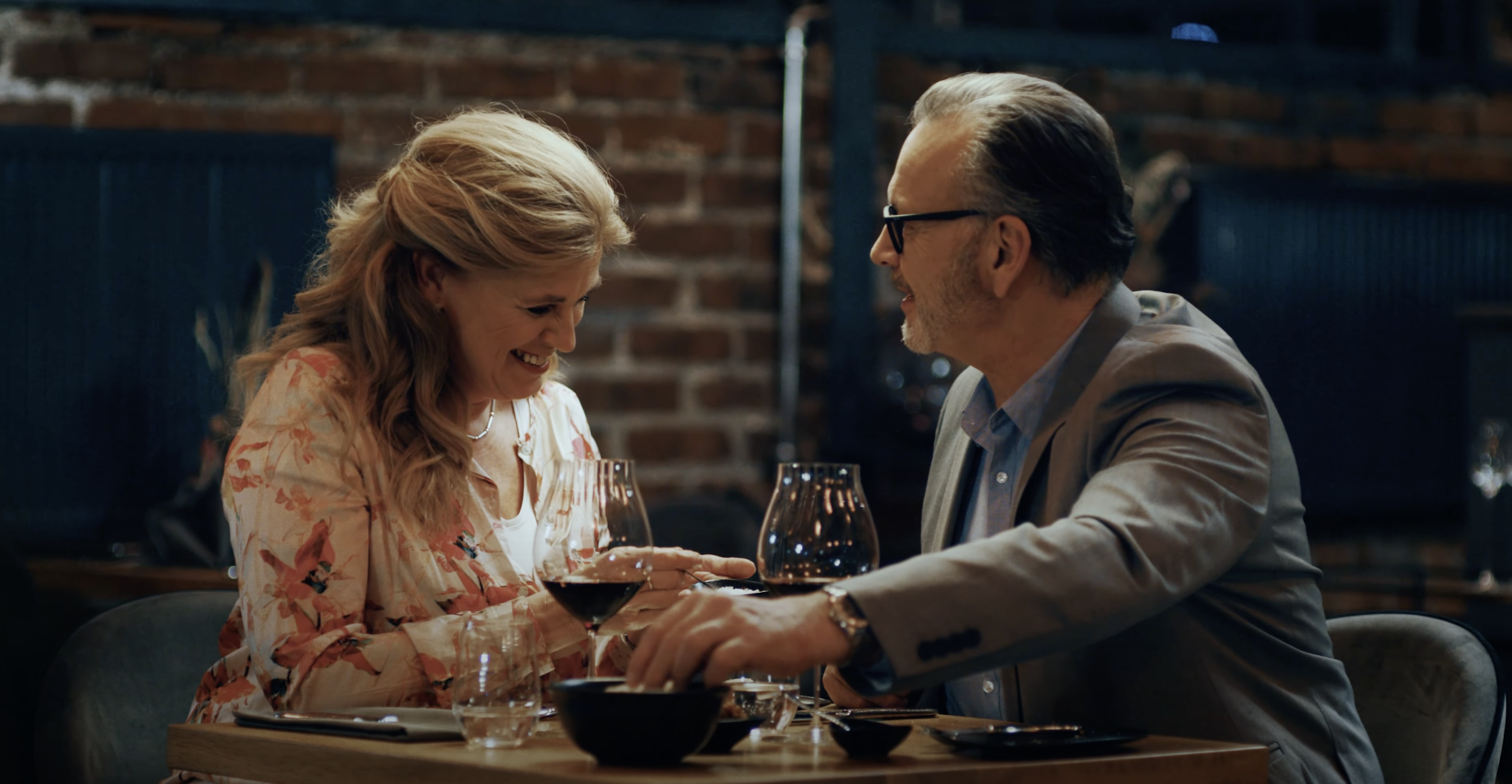 Ein Paar sitzt in einem stilvollen Restaurant bei Kerzenlicht, lacht und genießt ein Abendessen mit Wein – eine warme, romantische Stimmung.